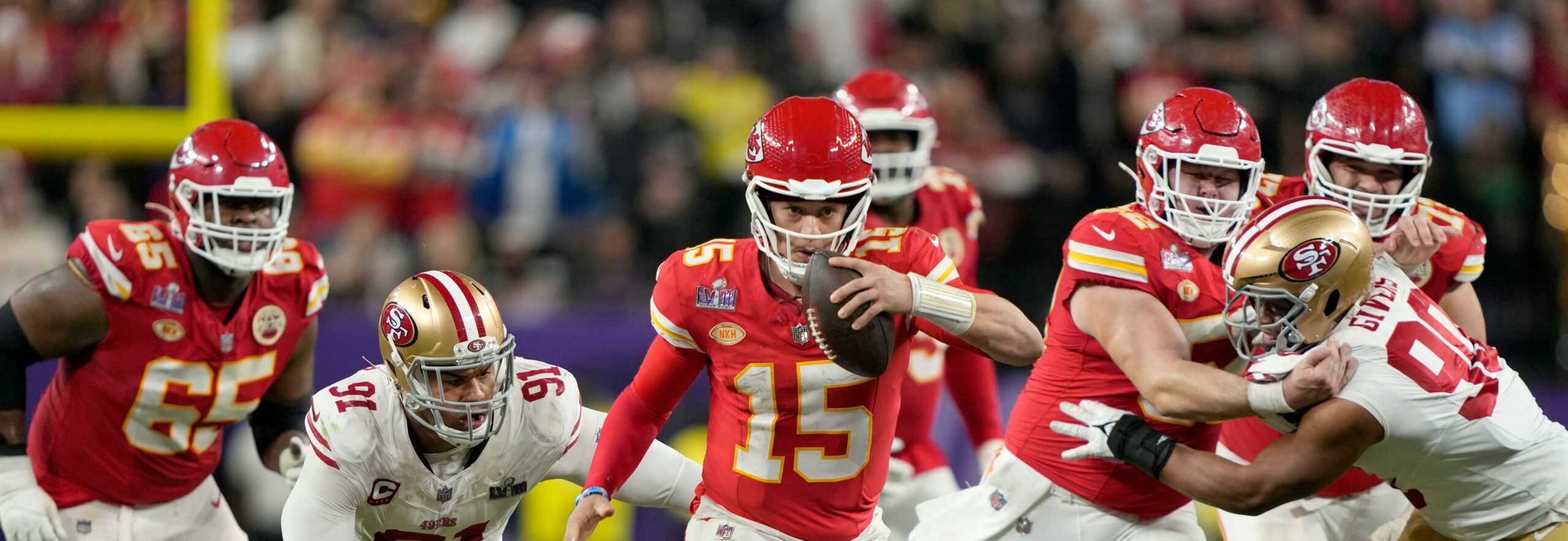 Patrick Mahomes (15), quarterback do Kansas City Chiefs, corre na prorrogação do jogo de futebol americano do Super Bowl 58 da NFL. O jogador usa uniforme vermelho com detalhes brancos e está rodeado pelos jogadores do seu time e do adversário.