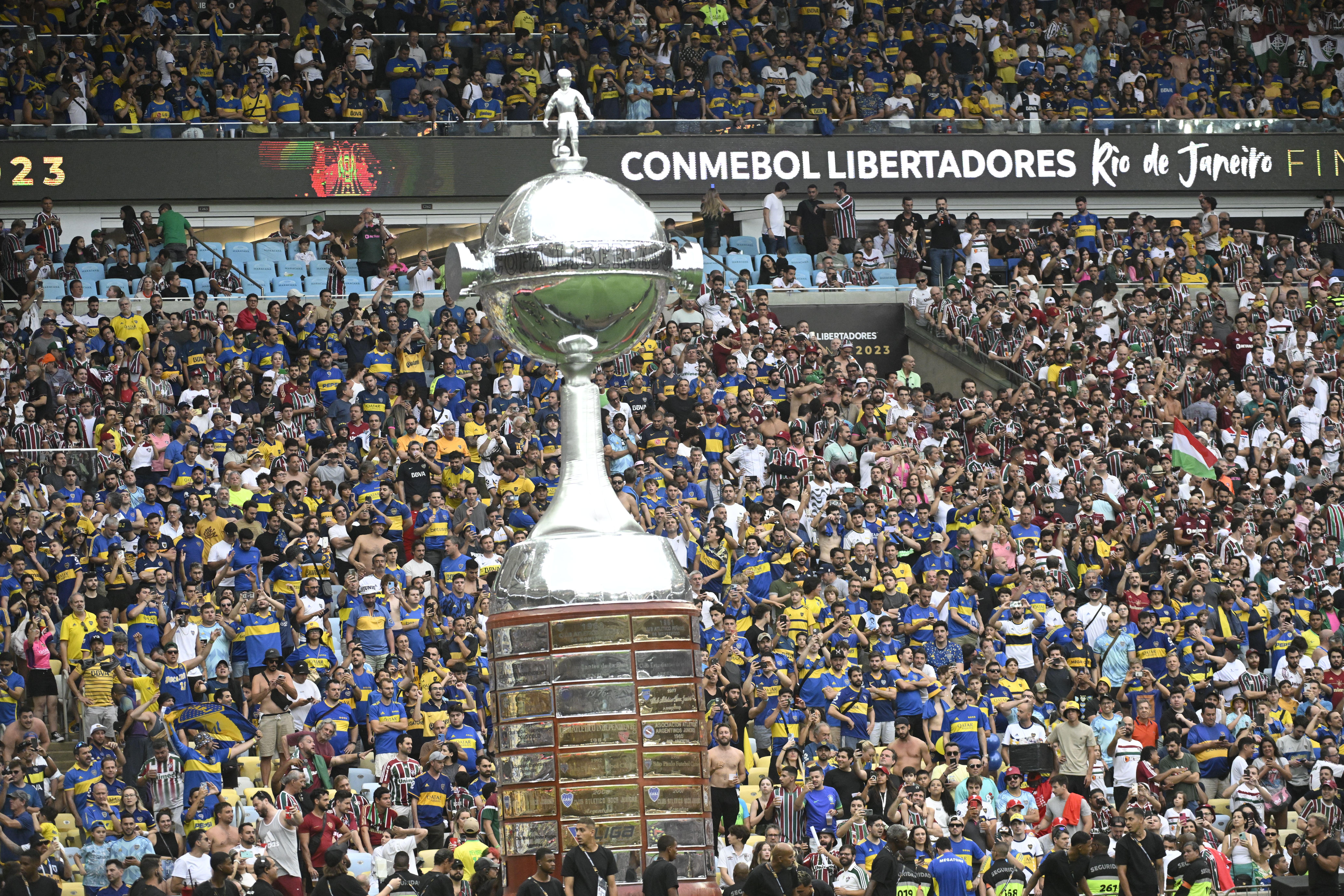 A imagem mostra a Taça da Libertadores de 2023, um troféu de prata imponente com detalhes em relevo. O troféu possui o nome "Taça Libertadores" gravado em sua base.