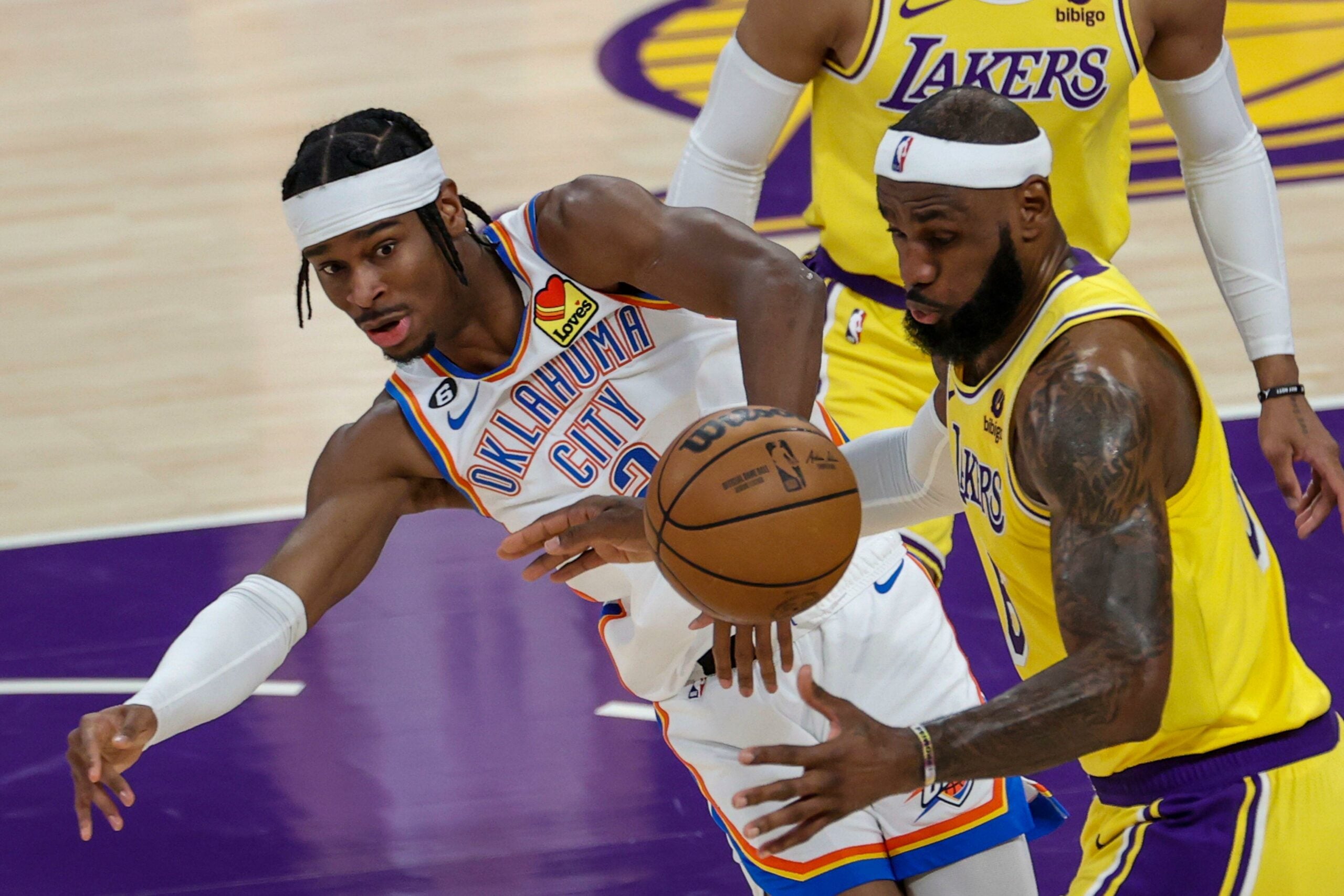 O armador do Oklahoma City Thunder, Shai Gilgeous-Alexander (E), e o ala do Los Angeles Lakers, LeBron James, disputam a bola durante uma partida de basquete da NBA.