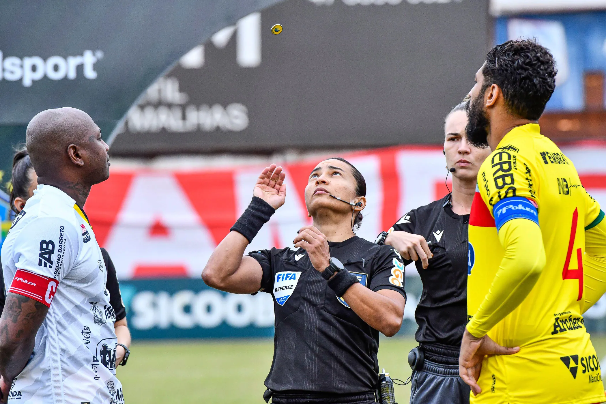Árbitra feminina lançando a moeda antes de uma partida de futebol entre Amazonas e Brusque, uma vestindo uma camisa branca e a outra uma camisa amarela, na final do campeonato da Série C.