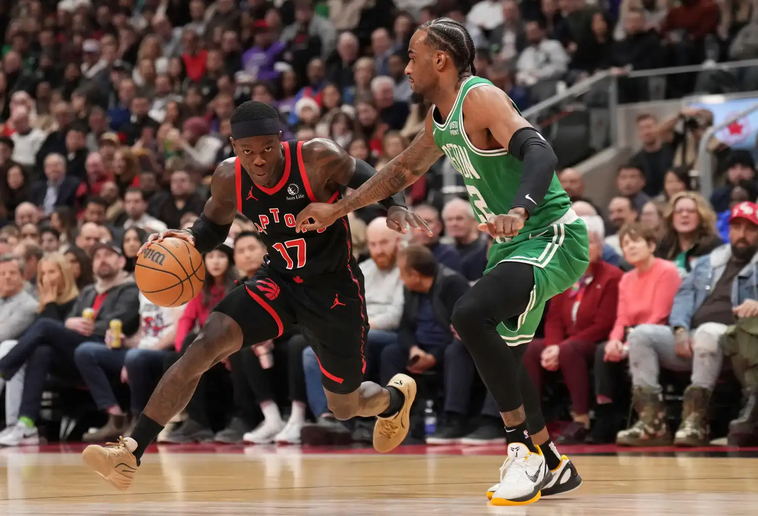 O armador do Toronto Raptors, Dennis Schroder (17), avança com a bola enquanto o ala do Boston Celtics, Oshae Brissett, à direita, defende durante o primeiro tempo do jogo de basquete da NBA em Toronto