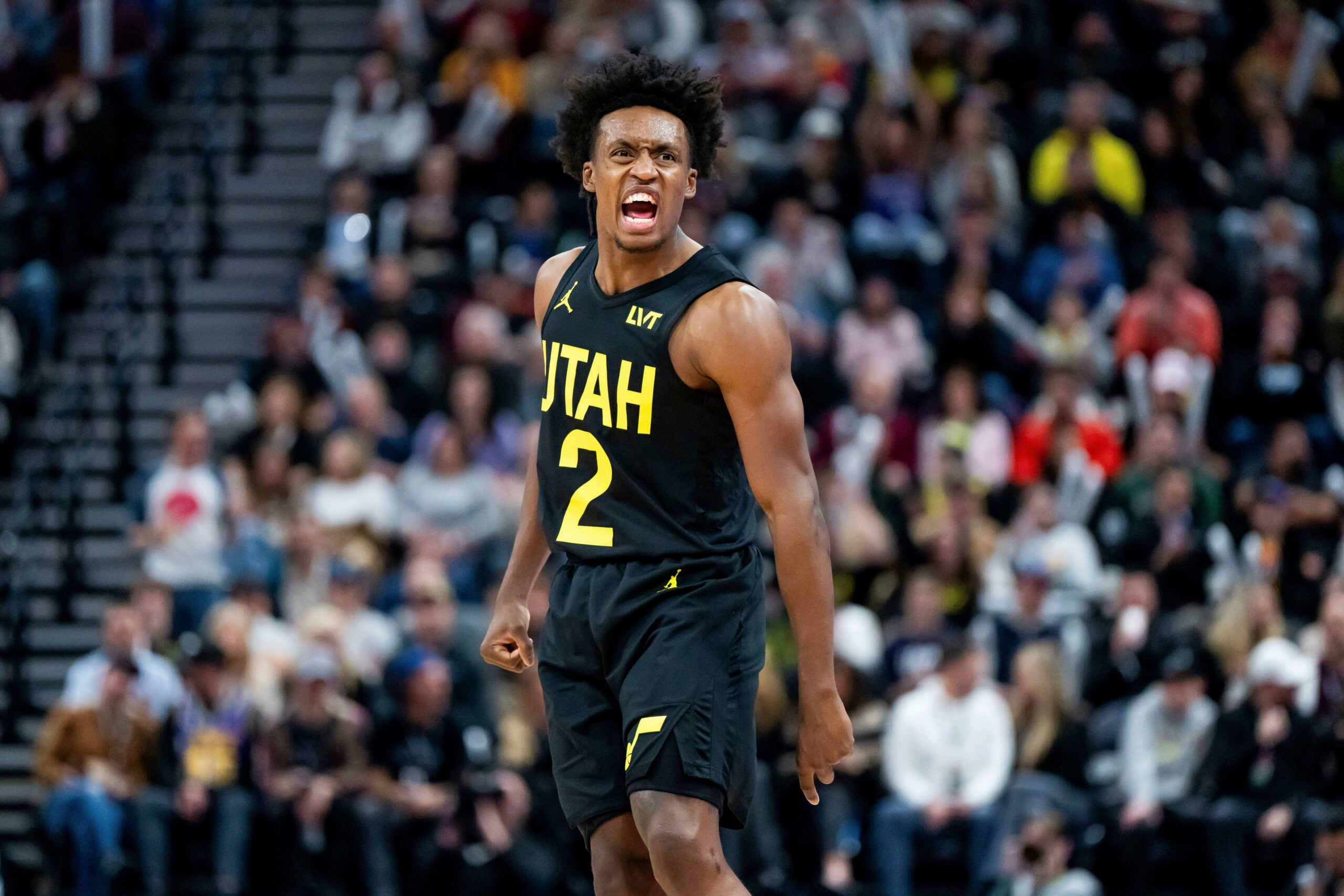 Jogador de basquete do Utah Jazz, vestindo uniforme preto número 2, expressa intensa emoção durante uma partida, com os espectadores desfocados ao fundo.