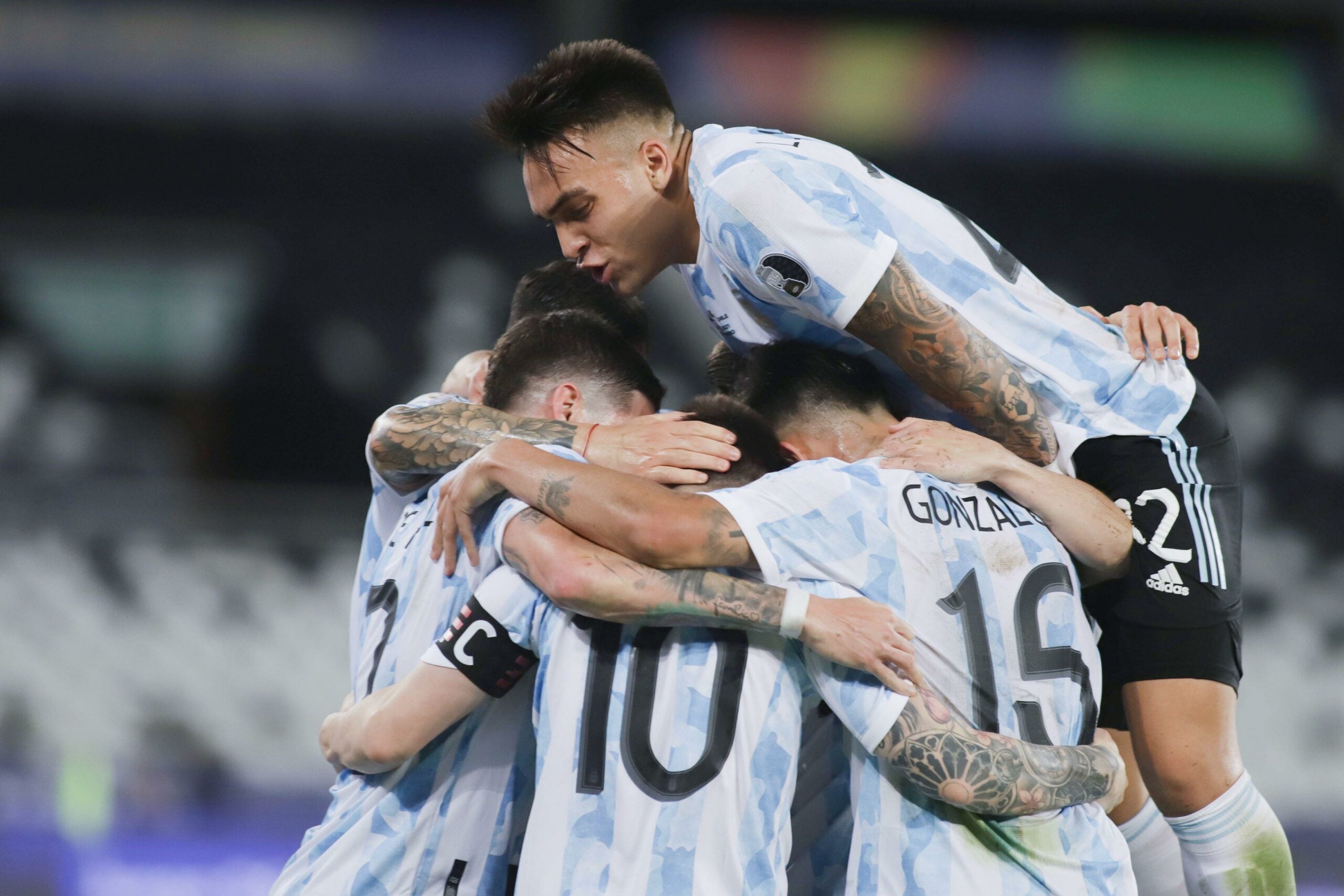 Jogadores da Argentina comemoram durante a partida do Grupo A entre Argentina e Chile na Copa América de 2021 em Brasília, Brasil, em 14 de junho de 2021. Eles usam uniforme azul com listras brancas e estão comemorando abraçados, sendo que um deles está por cima dos outros.