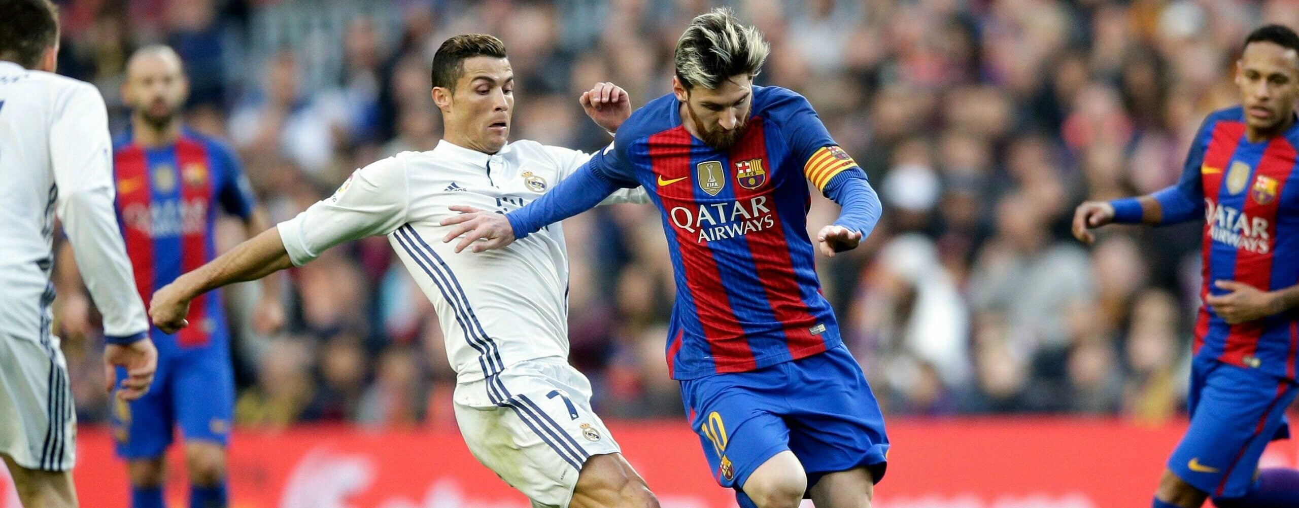 Lionel Messi do Barcelona, à direita do centro, escapa de Cristiano Ronaldo do Real Madrid durante a partida de futebol da La Liga espanhola entre o FC Barcelona e o Real Madrid no Camp Nou, em Barcelona, Espanha. Cristiano veste uniforme branco, cor do Real Madrid, enquanto Messi usa uniforme azul com listras vermelhas, do Barcelona. Messi domina a bola enquanto Cristiano Ronaldo tenta roubá-la.