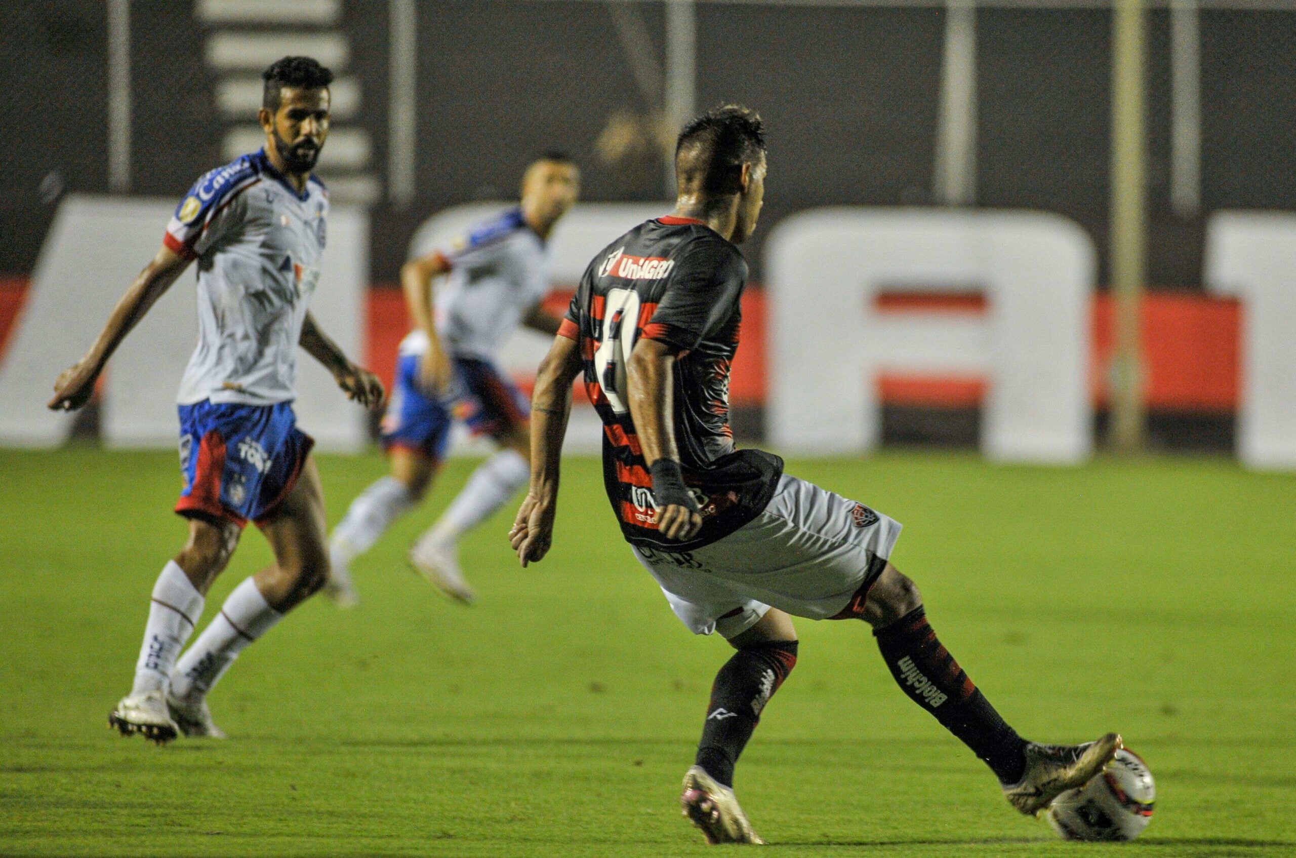 Jogador do Vitória, com a bola, sendo observado por um jogador do Bahia durante a partida no estádio Barradão pelo Campeonato Baiano 2022.
