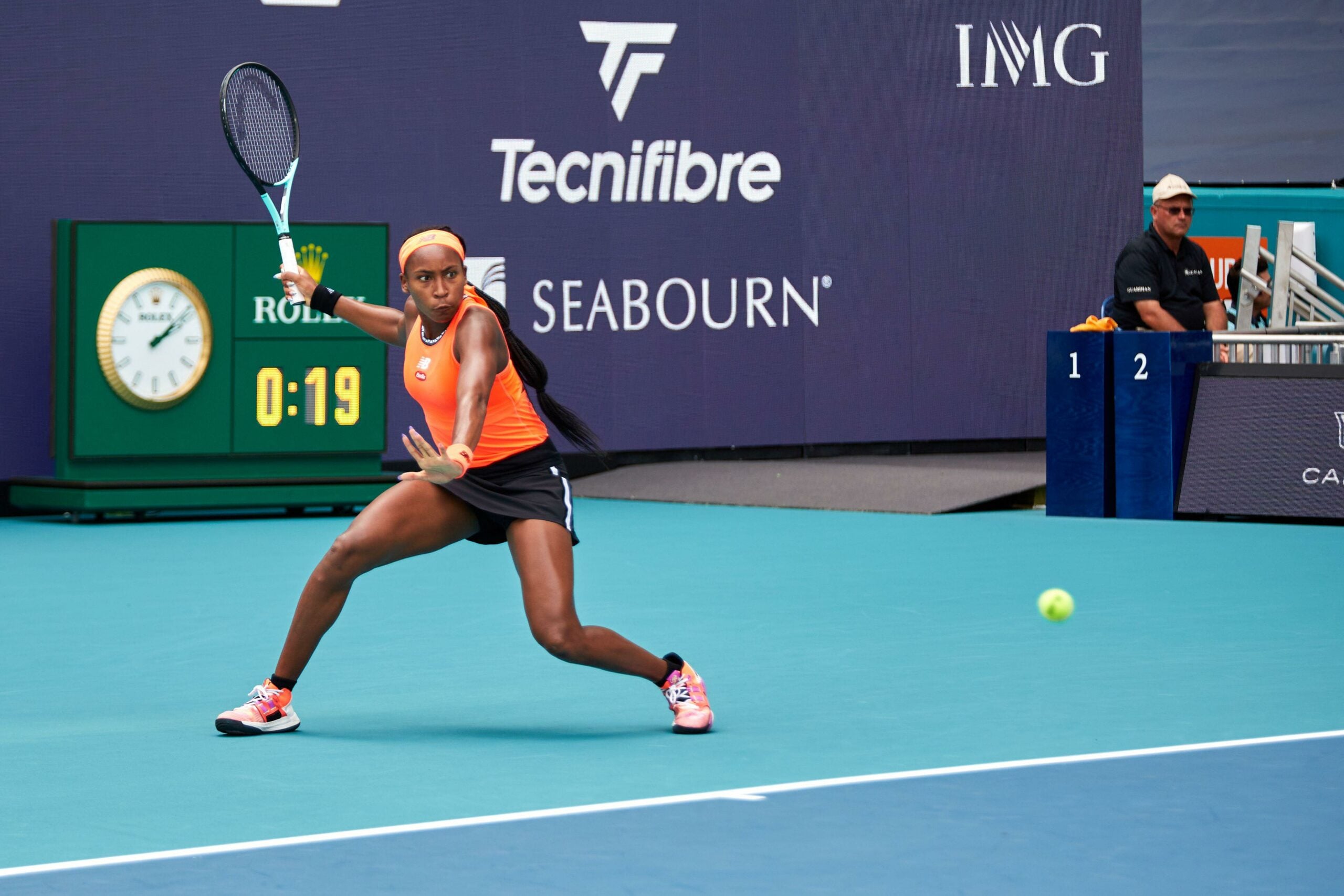 Foto de Coco Gauff, tenista norte-americana, em ação durante uma partida, vestindo roupa de jogo laranja e preta.