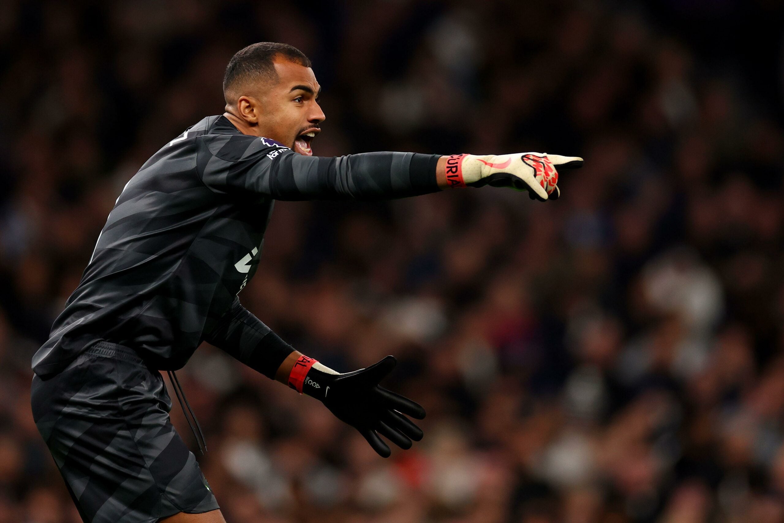 Robert Sánchez, goleiro, vestindo uniforme preto e luvas brancas com detalhes vermelhos, gesticulando e orientando seus companheiros durante uma partida.