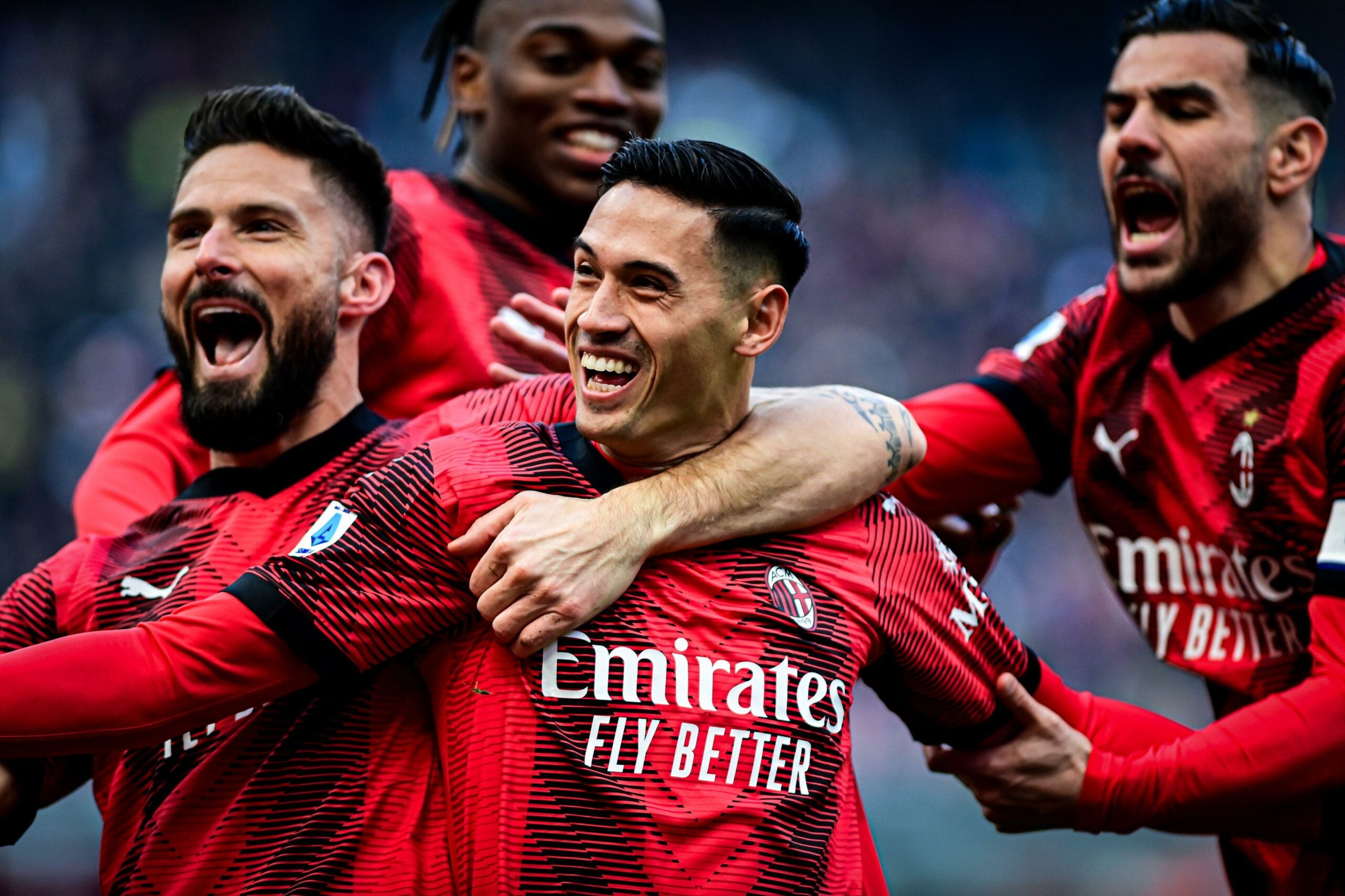 Tijani Reijnders e Olivier Giroud, do AC Milan, comemoram após marcar o primeiro gol de sua equipe durante a partida de futebol da Serie A italiana AC Milan vs Monza, no Estádio San Siro, em Milão, Itália. Os jogadores usam uniforme vermelho com listras pretas e demonstram expressão de alegria. Olivier Giroud abraça o jogador Tijani Reijnders em comemoração, enquanto outro jogador está atrás deles, também celebrando o gol.