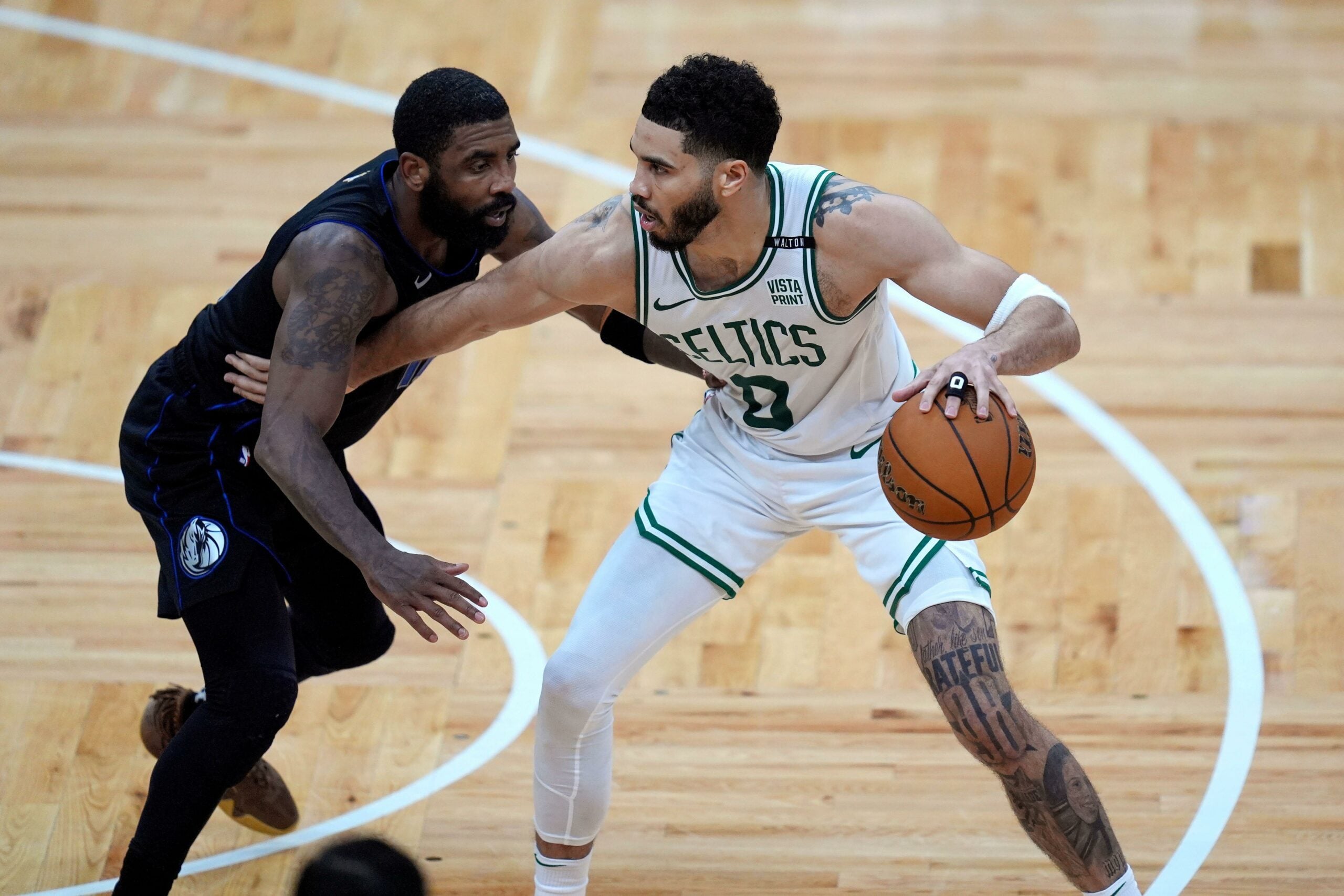 A imagem retrata um jogo acirrado entre os times de basquete Boston Celtics e Dallas Mavericks. Os jogadores estão em diferentes posições, alguns driblando, passando ou arremessando a bola.