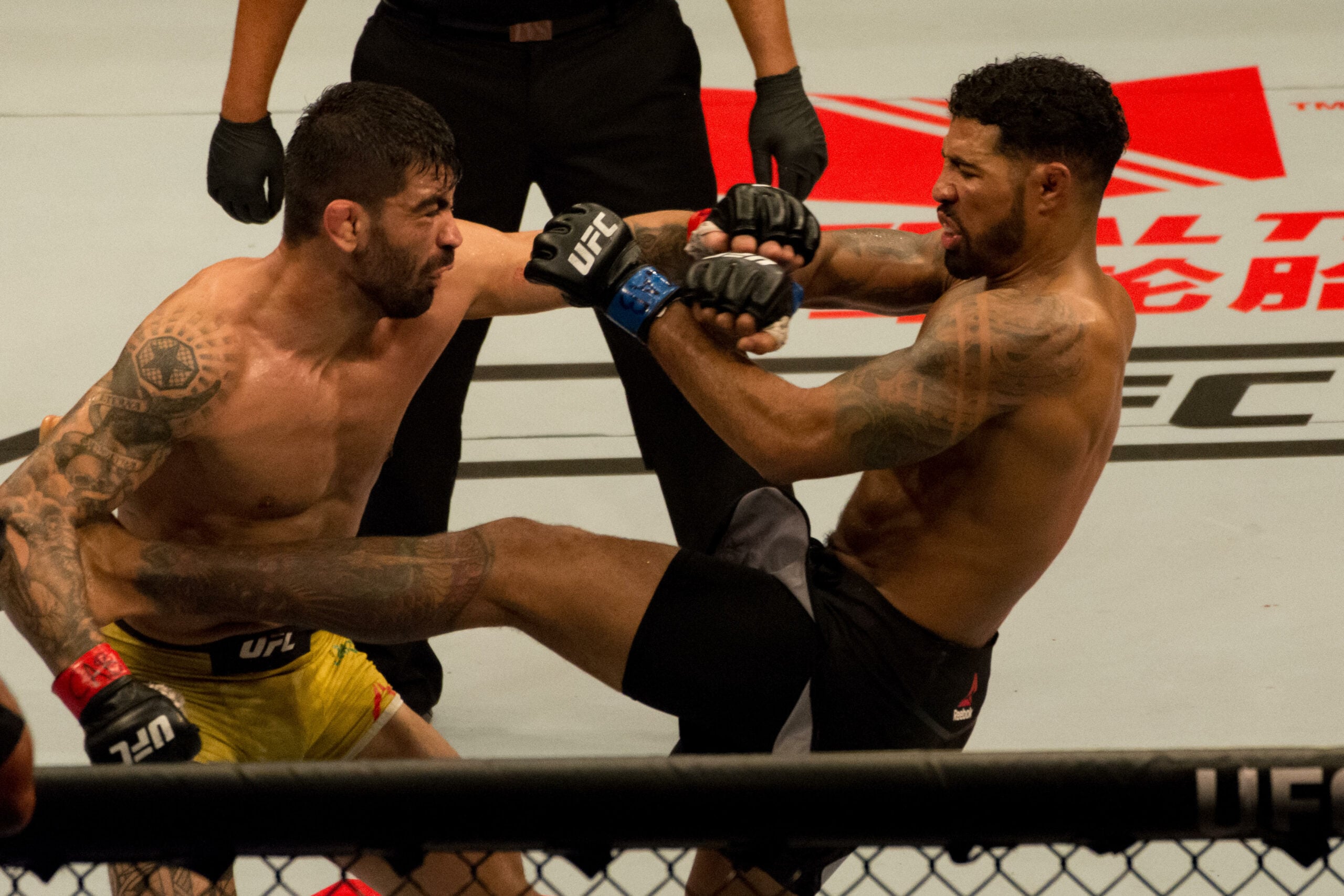 O meio-campista Elizeu (Capoeira) Zaleski dos Santos e Max Griffin durante o UFC Fight Night - Brunson vs Machida no Ginásio do Ibirapuera em São Paulo. Os lutadores estão aplicando golpes enquanto o juiz surge atrás dentro do ringue.