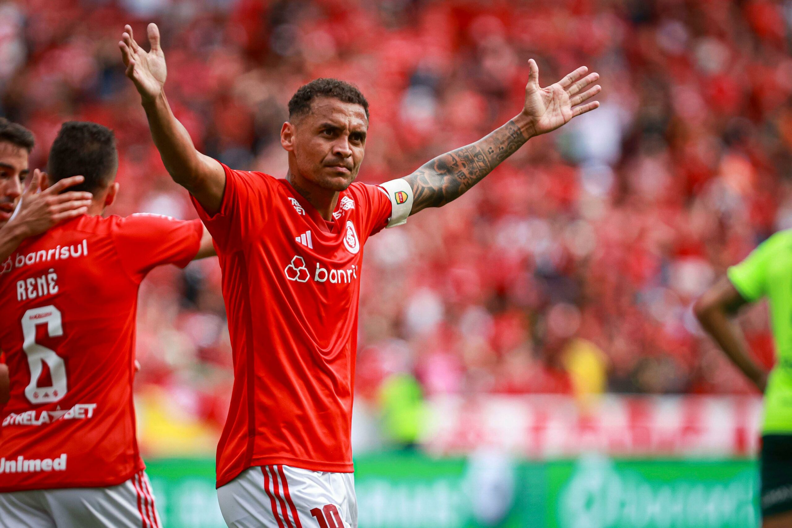 Jogador de futebol do Internacional, vestindo a camisa vermelha número 10, erguindo os braços em celebração durante uma partida